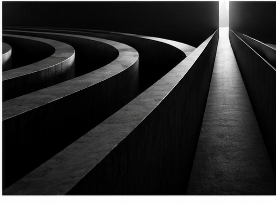 Dark architectural pathways opening toward a narrow lighted route